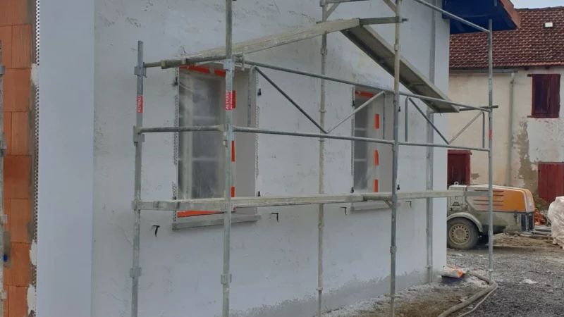 Application de l’enduit blanc sur le pignon d’une maison neuve depuis un échafaudage.