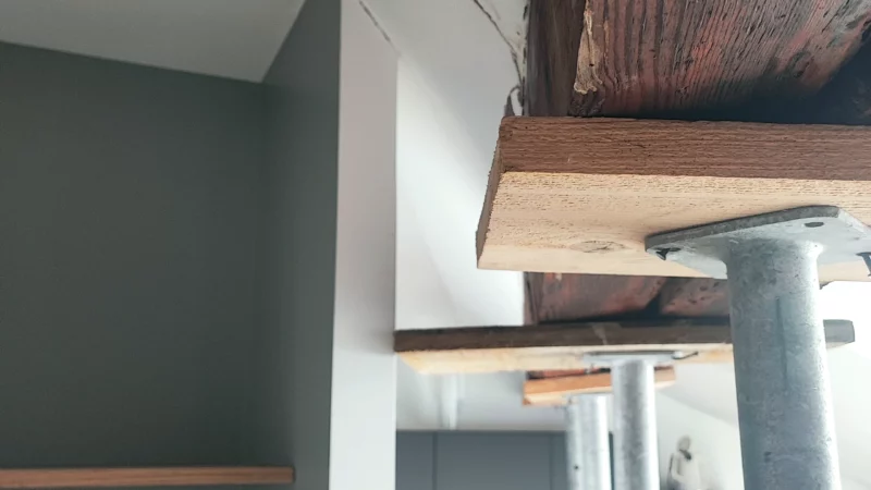 Appui d’un étai métallique sous une poutre en bois à l’intérieur du bâtiment.