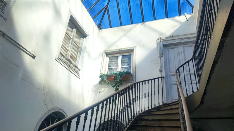 Cage d'escalier ancienne éclairée par une verrière et entourée de fenêtres cintrées.