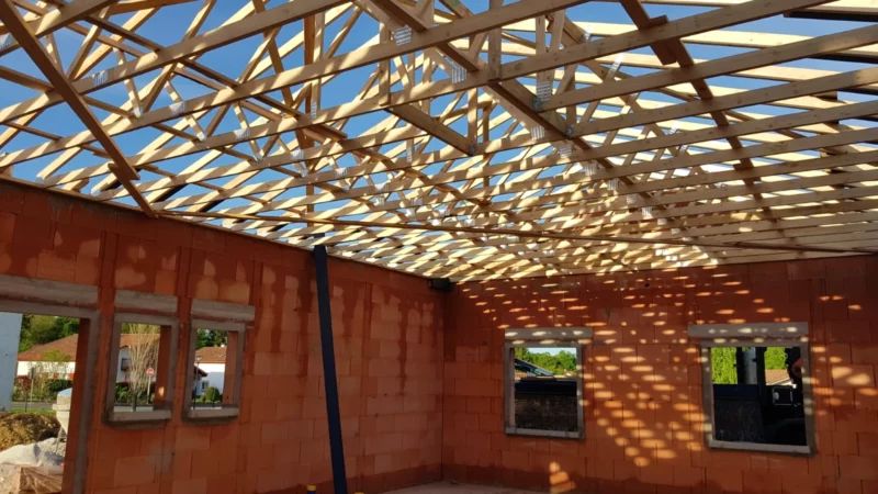 Vue intérieure d’une charpente en fermettes bois posée sur les murs en briques d’une maison neuve.