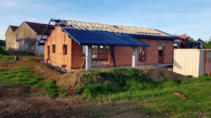 Vue extérieure d’une maison neuve en briques pendant la pose de la charpente et de la toiture.