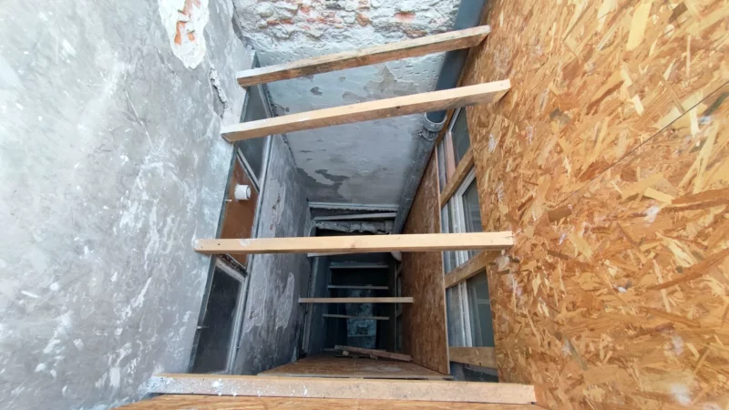 Cour intérieure étroite protégée par des panneaux OSB et des traverses en bois.