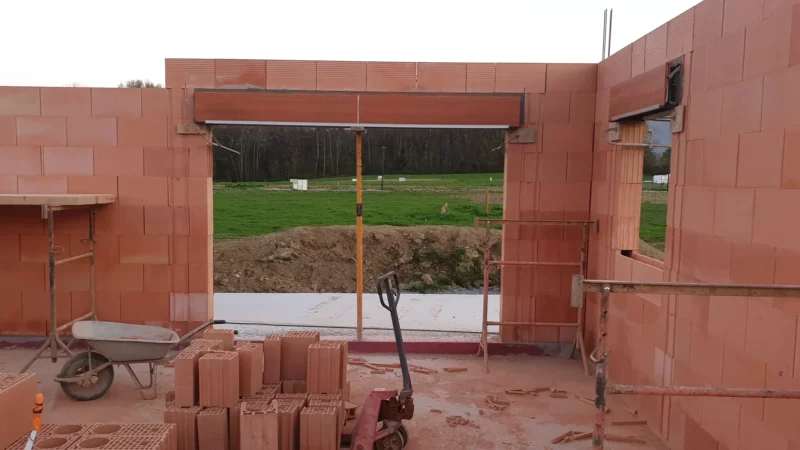 Élévation des murs en briques autour d’une grande baie vitrée de maison neuve.