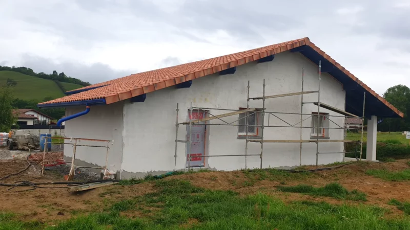 Façade pignon d’une maison neuve avec enduit blanc en cours et échafaudage.