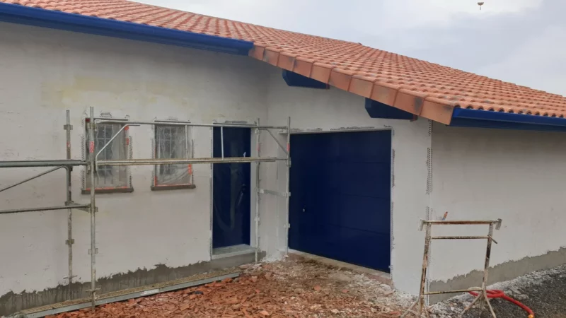 Façade de maison neuve enduite avec porte d’entrée et porte de garage sectionnelle.