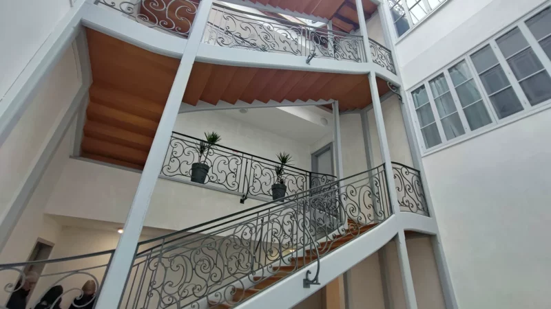 Escalier intérieur à marches en bois et garde-corps ouvragés dans une cage d'escalier couverte.