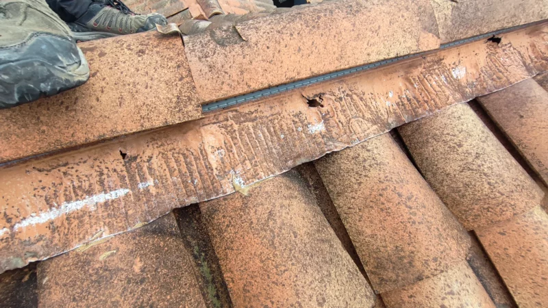 Bande d’étanchéité dégradée sous les tuiles faîtières d’une toiture.