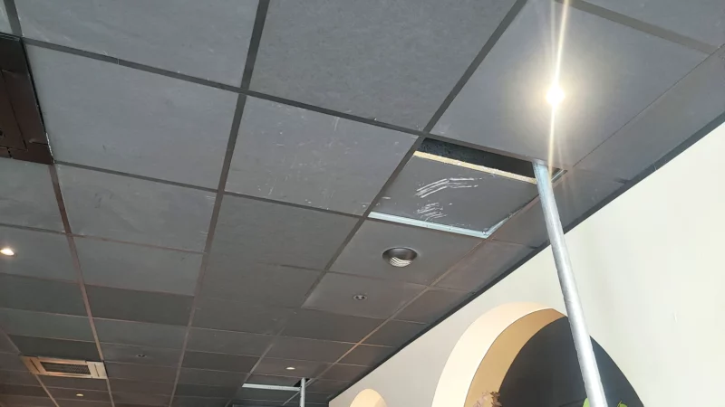 Faux plafond démonté partiellement et soutenu par des étais dans un local commercial.