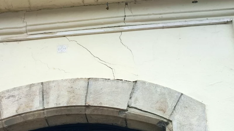Fissures autour d’une arche en pierre et sous un balcon en façade.