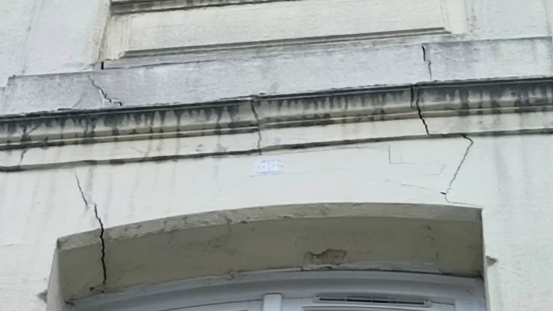 Fissures visibles sur la façade entre deux fenêtres d’un immeuble ancien.