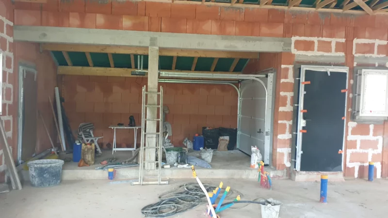 Intérieur d’un garage de maison neuve avec porte sectionnelle et réseaux techniques en attente.