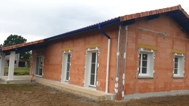 Maison neuve en briques avec toiture en tuiles, gouttières et menuiseries extérieures posées.