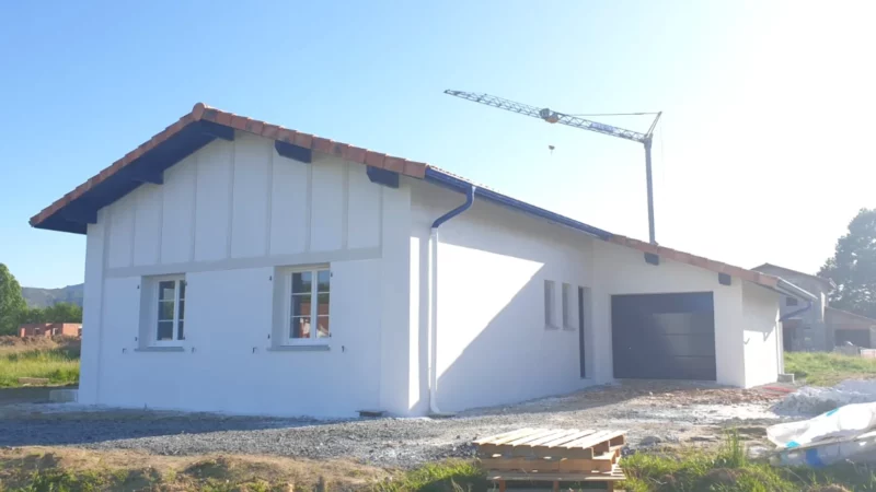 Maison neuve enduite en blanc avec toiture en tuiles et porte de garage.