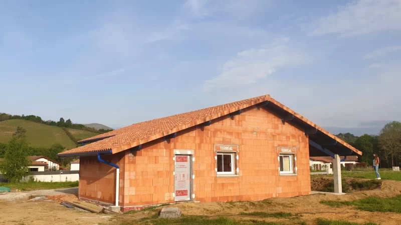 Façade latérale d’une maison neuve en briques après la pose de la toiture en tuiles.