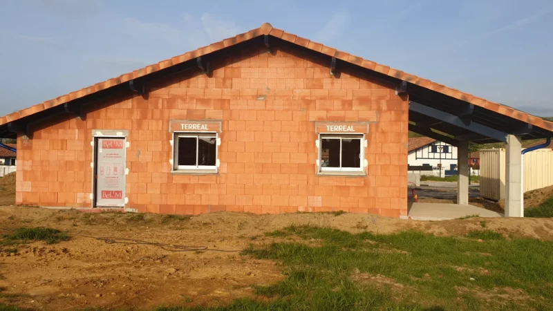 Façade pignon d’une maison neuve en briques avec toiture en tuiles et terrasse couverte.