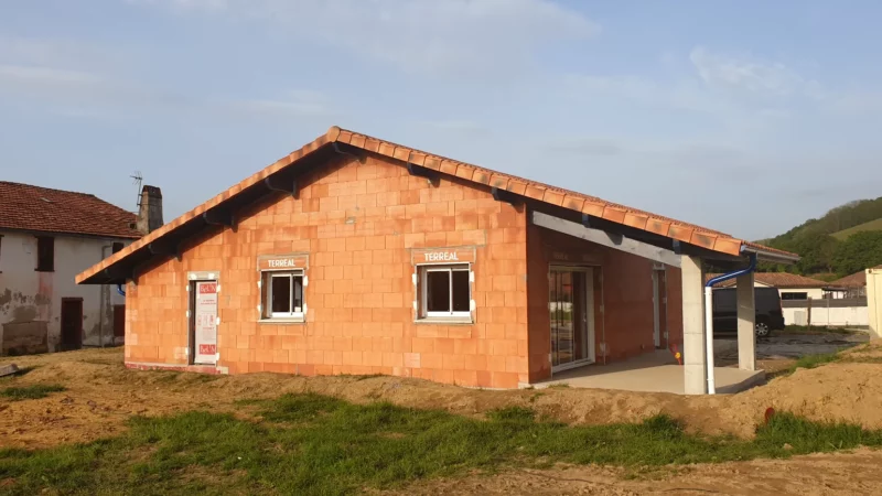 Maison neuve en briques avec toiture en tuiles et avancée formant une terrasse couverte.