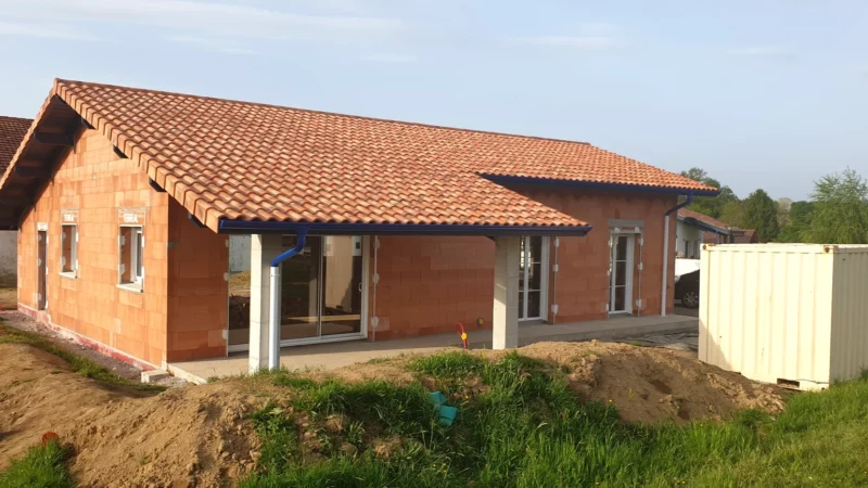 Vue générale arrière d’une maison neuve en briques avec toiture en tuiles et terrasse couverte.