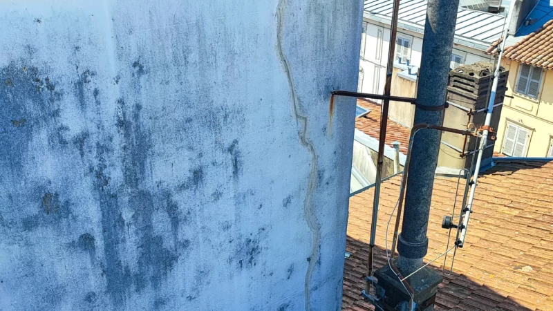 Mur pignon en toiture présentant des traces d'humidité et une fissure verticale.