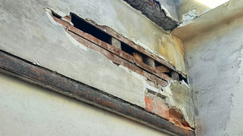 Ossature en bois mise à nu dans un mur ancien sous une verrière.