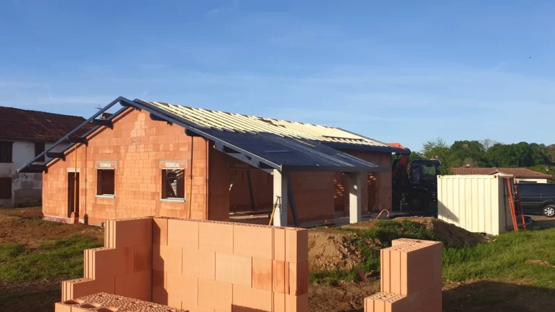Maison neuve en briques pendant la pose de la charpente et de l’écran sous-toiture.