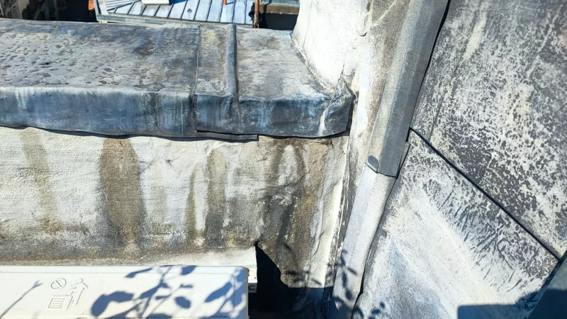 Raccord entre un mur et un ouvrage en zinc présentant des traces de ruissellement.