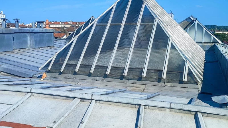 Vue générale d'une grande verrière pyramidale au milieu des couvertures en zinc.