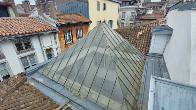 Vue d'ensemble de la verrière pyramidale au milieu des toitures anciennes.
